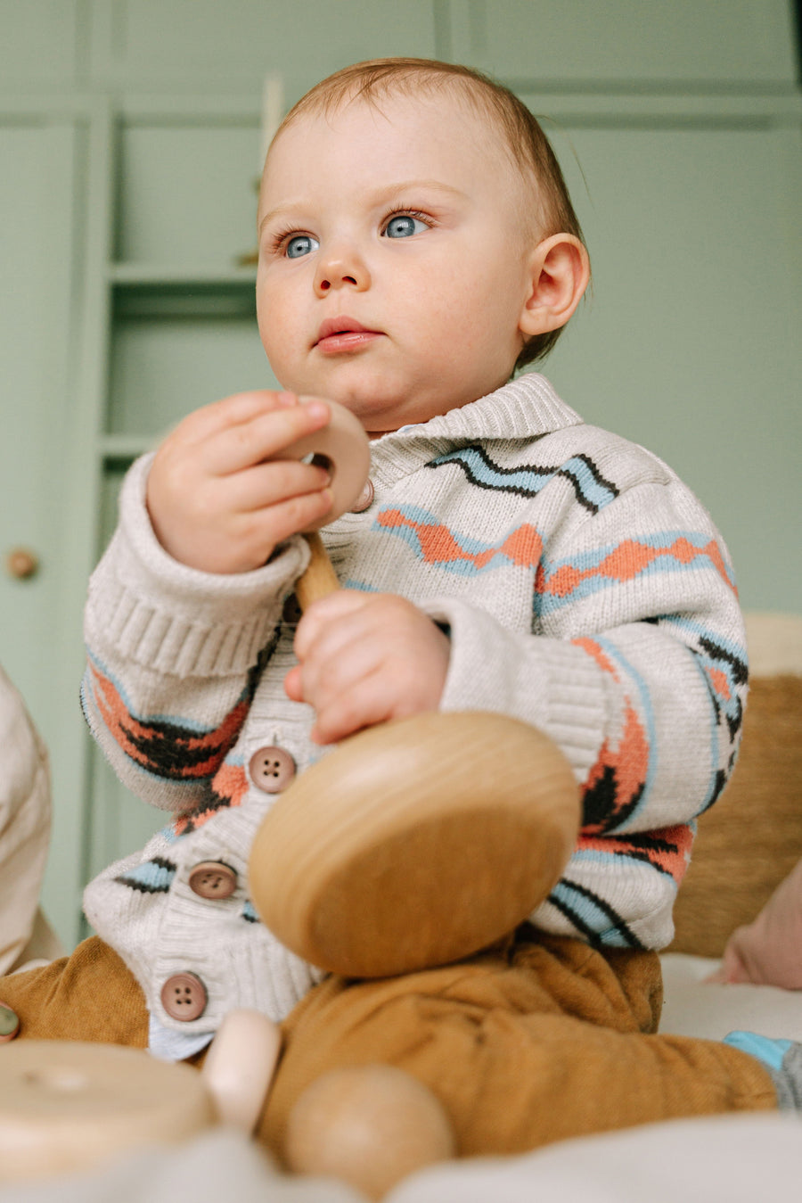 Baby sitting indoors and playing with a colourful wooden toy