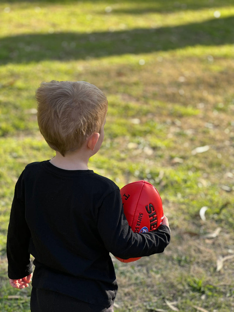 Young child holding an Australian football in a sunny Victorian park.