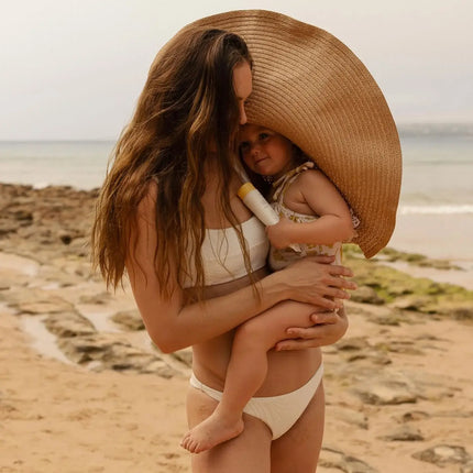 Woman holding a child on a beach with a large straw hat